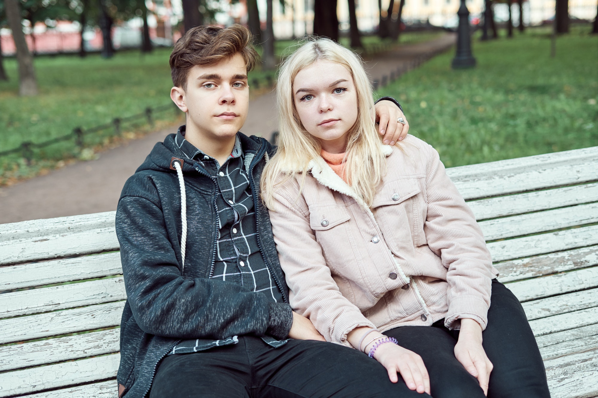 Teenagers in love sit on park bench in autumn, looking straight ahead